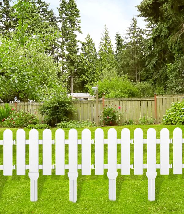 A charming white picket fence encloses a yard adorned with vibrant green trees, enhancing the serene landscape.