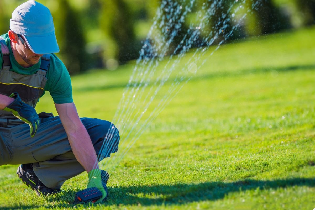 A man using a hose to water his green lawn on a sunny day, ensuring the grass remains healthy and vibrant.